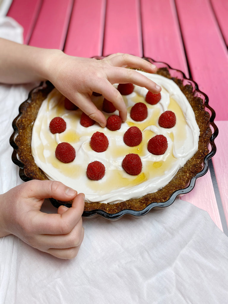 yogurt and berry tart with a GF pecan crust on a pink table with a child's hands