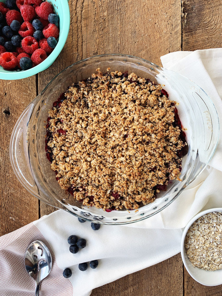 Healthy mixed berry crisp in a pie pan with fresh berries on the side.