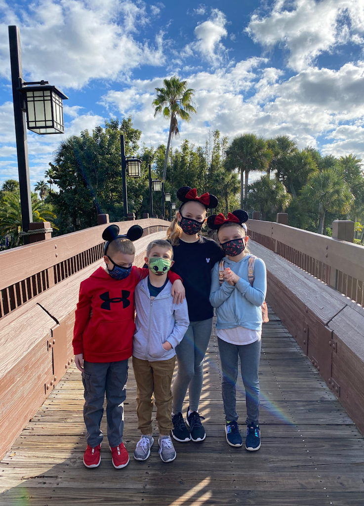 four kids on a bridge at a Disney Resort with Mickey ears on