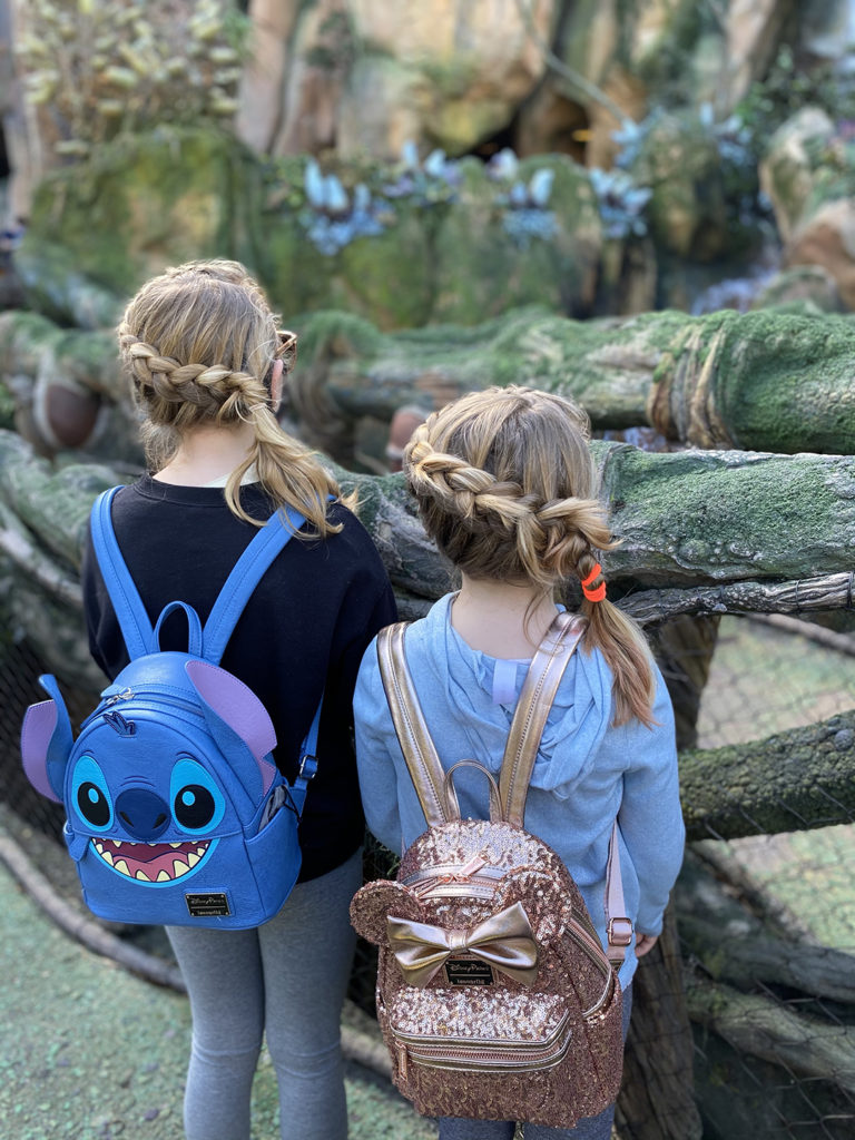 two girls with braids in their hair wearing Disney mini backpacks.